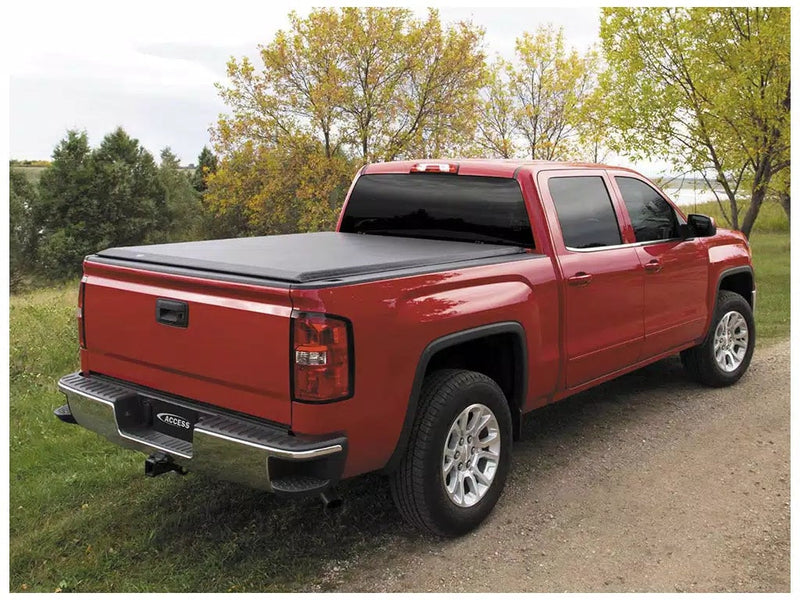 Access Original roll-up tonneau cover on a pickup bed: red crew cab pickup on a dirt track with a black roll-up cover closed over the bed (trailer hitch receiver shown, not included)