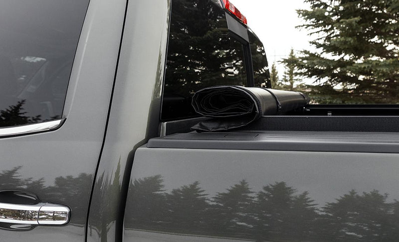 Close-up of the Access Original roll-up tonneau cover: rolled vinyl tonneau cover strapped against the cab on a gray pickup's side rail