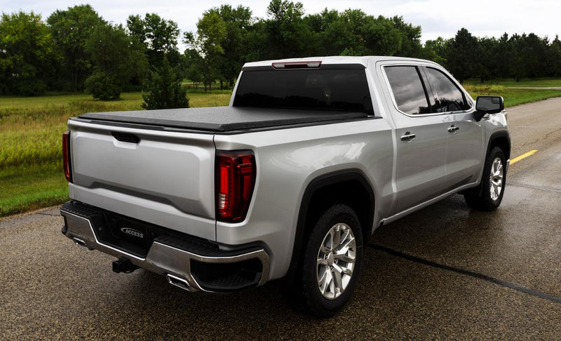 Access Original roll-up tonneau cover on a pickup bed: silver crew cab pickup on wet pavement with a black roll-up cover closed over the bed, rear three-quarter view (trailer hitch receiver shown, not included)