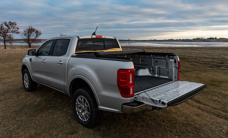 Access Original roll-up tonneau cover on a pickup bed: silver pickup by a lake with the roll-up cover rolled to the cab, tailgate down, carpet mat in the bed (bed mat shown, not included)