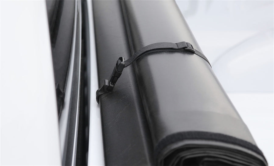 Access roll-up tonneau cover: Close-up of a rolled black vinyl cover held by a nylon storage strap and clip at the bulkhead