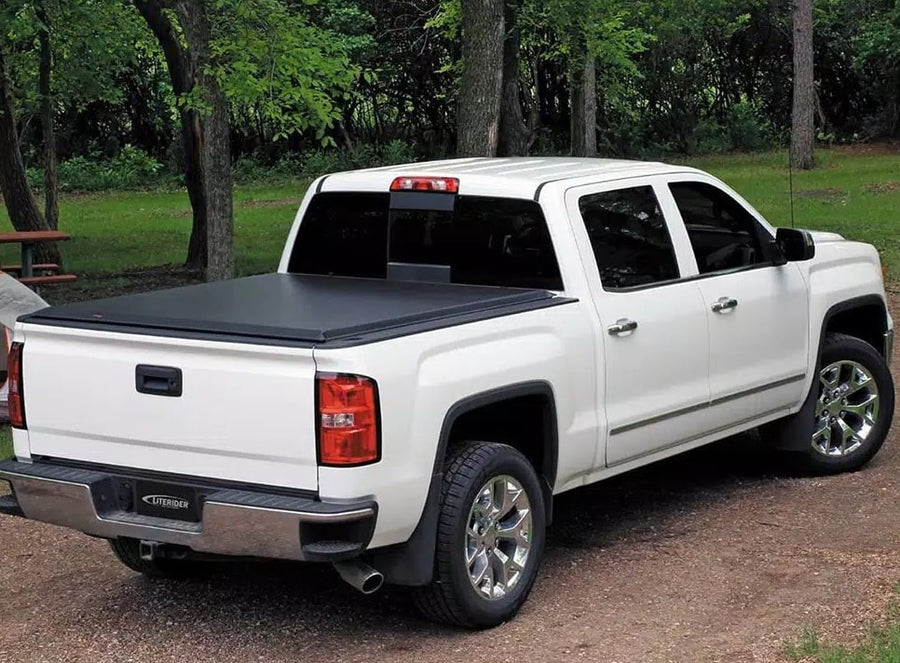 Access LiteRider roll-up tonneau cover: White crew-cab pickup at a wooded campsite with a black roll-up cover closed over the bed
