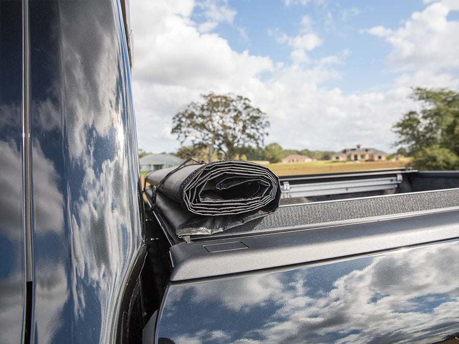 Access LiteRider roll-up tonneau cover: Black vinyl roll-up cover rolled tight against the cab and held by storage straps, viewed along the bed rail