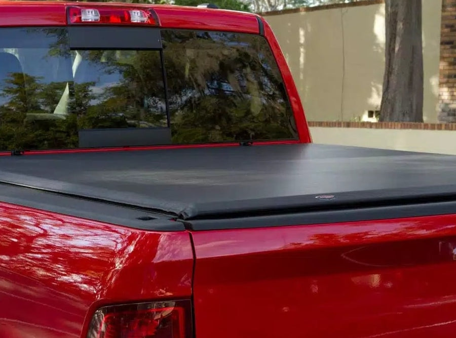 Access Lorado roll-up tonneau cover: Close view of a black roll-up cover closed over a red pickup bed, rear corner and cab window visible