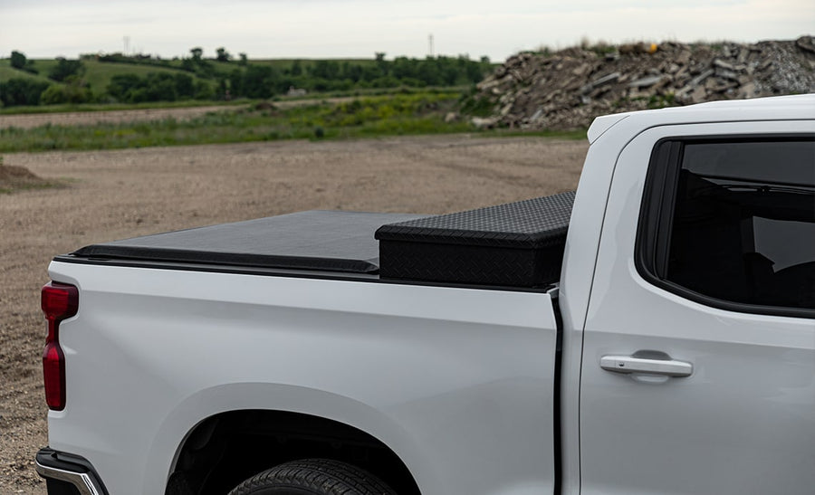 Access Toolbox Edition roll-up tonneau cover: Side close-up of a black roll-up cover closed on a white pickup, ending at a black diamond-plate bed toolbox