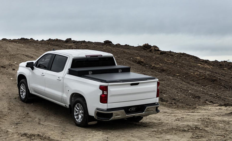 Access Toolbox Edition roll-up tonneau cover: White crew cab pickup on a dirt hill, black roll-up cover closed behind a black bed toolbox