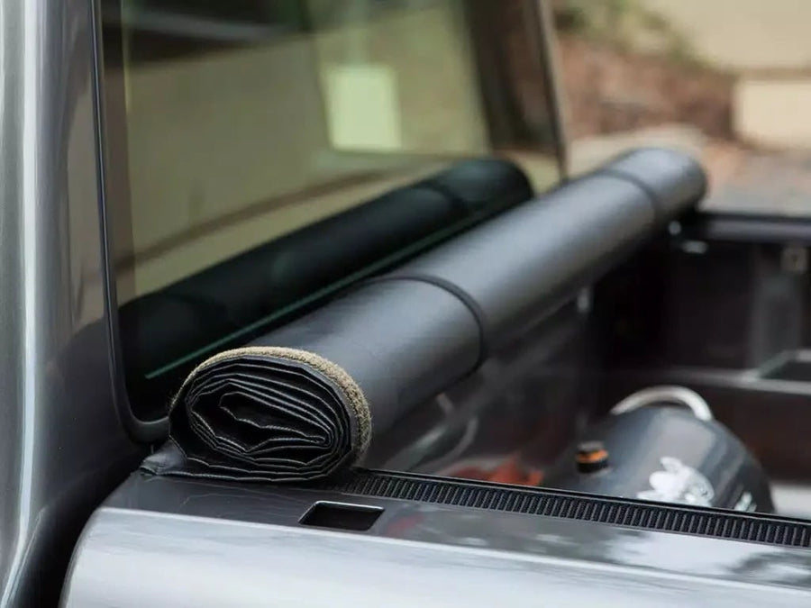 Access Vanish roll-up tonneau cover: Close-up of a black vinyl cover rolled and strapped at the cab end of a pickup bed, cargo visible beyond