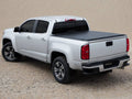 Silver crew cab midsize pickup on sand with a black roll-up tonneau cover closed flat over the bed