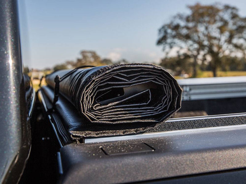 Vinyl roll-up cover rolled at the cab and held by storage straps, seen along the bed rail
