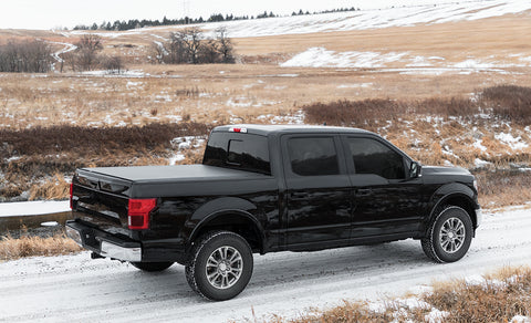 Access TonnoSport roll-up tonneau cover on a pickup bed: black crew cab pickup on a snowy prairie road with a roll-up cover closed over the bed