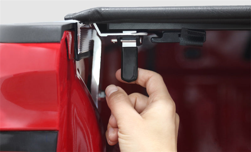 Close-up of the Access TonnoSport roll-up tonneau cover: hand pulling the trigger latch under the rear edge of a roll-up cover on a red pickup