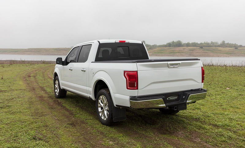 Access TonnoSport roll-up tonneau cover on a pickup bed: white crew cab pickup on a grassy track with a roll-up cover closed over the bed