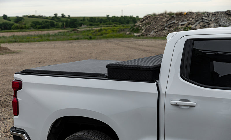 Access Toolbox Edition roll-up tonneau cover on a pickup bed: side close-up of a black roll-up cover closed on a white pickup, ending at a black diamond-plate bed toolbox (truck-bed toolbox shown, not included)