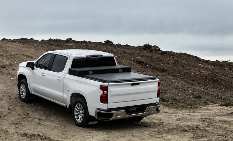 Access Toolbox Edition roll-up tonneau cover on a pickup bed: white crew cab pickup on a dirt lot, black roll-up cover closed behind a black bed toolbox (truck-bed toolbox shown, not included)
