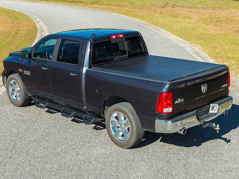 Elevated rear three-quarter view of a black soft roll-up cover closed over the bed of a dark pickup on a curved road