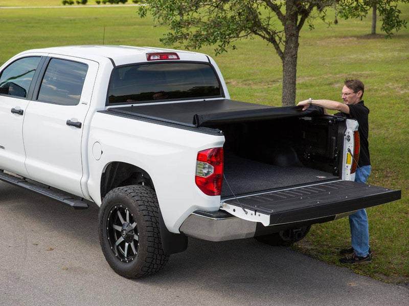 Man at the open tailgate rolling the soft cover forward toward the cab, bed partly uncovered