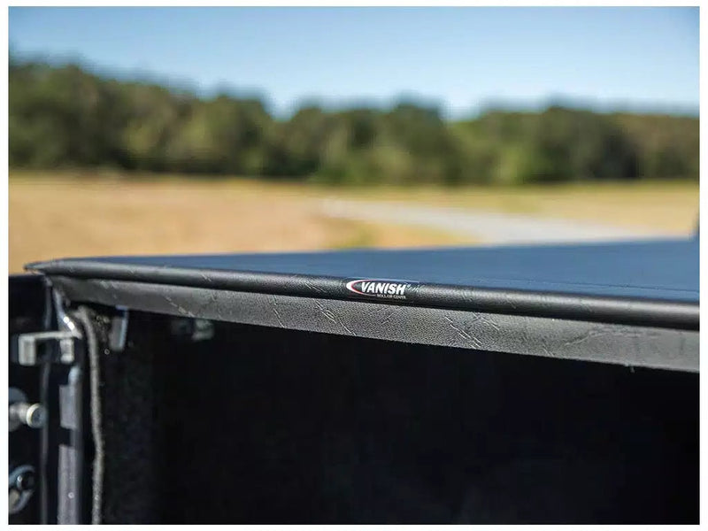 Close-up of the Access Vanish roll-up tonneau cover: close-up of a black roll-up cover rear edge with a small logo, closed over a carpeted pickup bed (carpeted bed liner shown, not included)