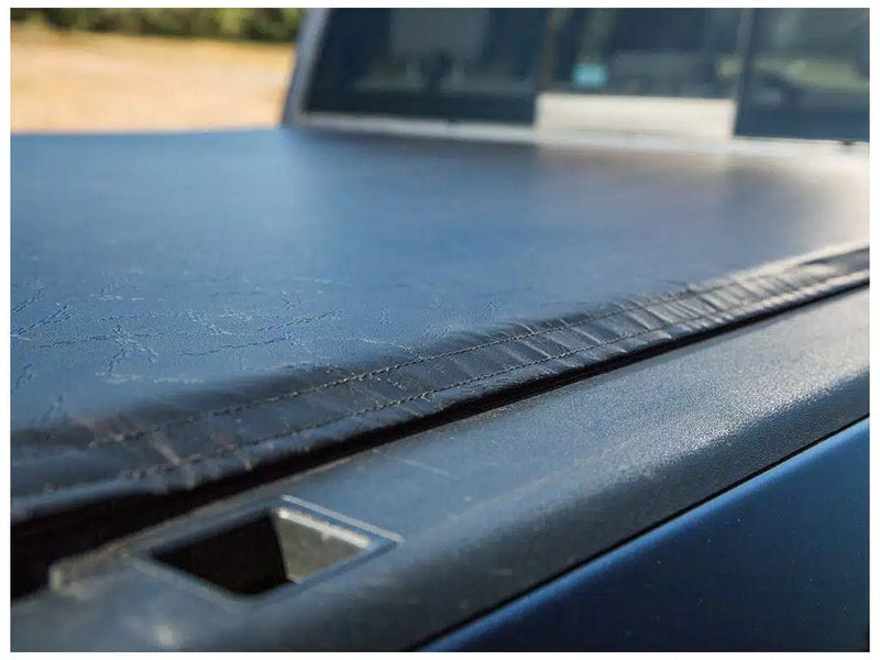 Close-up of the Access Vanish roll-up tonneau cover: close-up of a black vinyl roll-up cover edge closed over the bed rail of a dark pickup