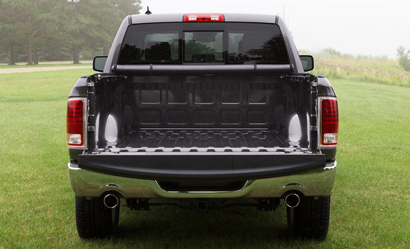 Access Vanish roll-up tonneau cover on a pickup bed: rear view of a dark pickup on grass with the cover rolled to the cab and tailgate down, empty lined bed (bedliner shown, not included)