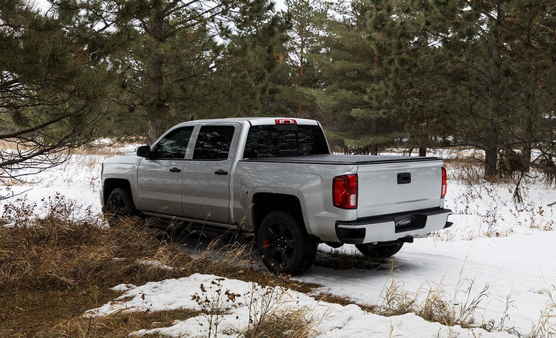 Access Vanish roll-up tonneau cover on a pickup bed: silver crew cab pickup in snowy pines, black low-profile roll-up cover closed over the bed