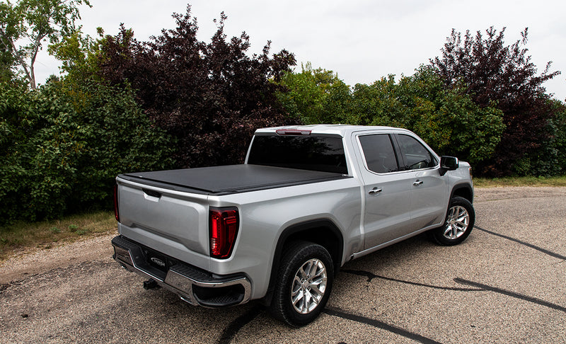 Access Vanish roll-up tonneau cover on a pickup bed: silver crew cab pickup on a paved lot, black low-profile roll-up cover closed over the bed