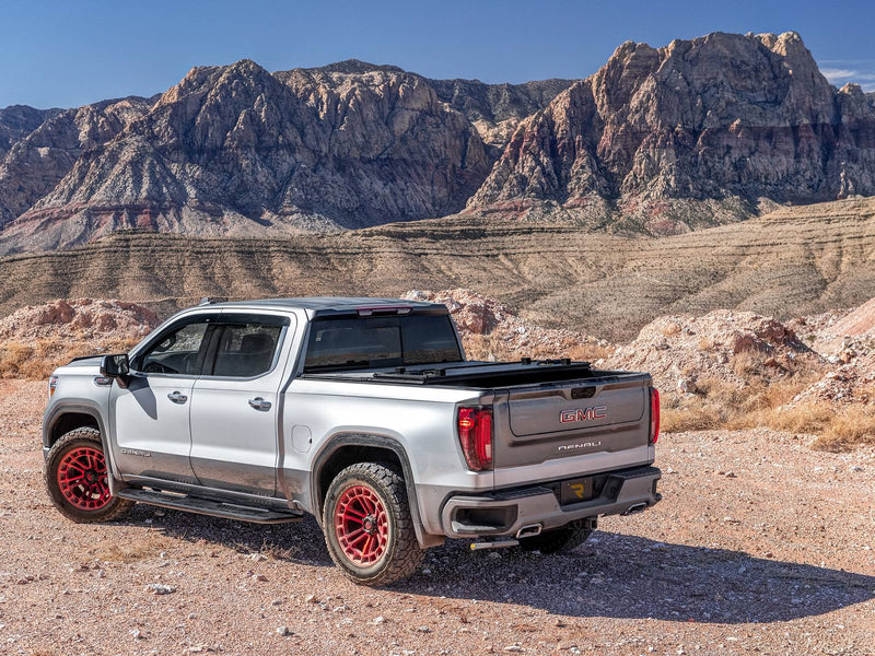 Silver crew-cab pickup with red wheels parked in a desert canyon, bed step stowed under the rear bumper