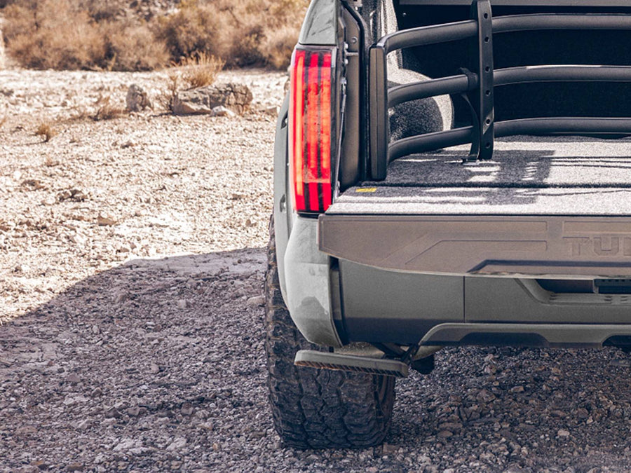 Rear corner of a pickup on gravel with the tailgate down, a bed extender in the bed and the step deployed under the bumper
