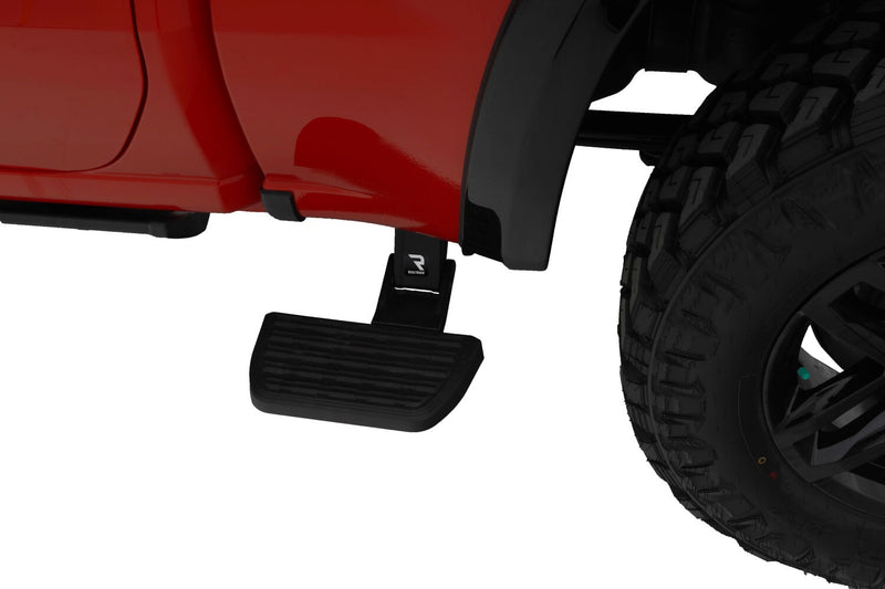 Side bed step deployed ahead of the rear wheel of a red pickup, studio background