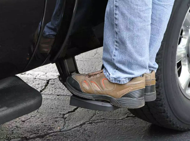 Work shoes on the deployed side bed step ahead of the rear wheel of a dark pickup
