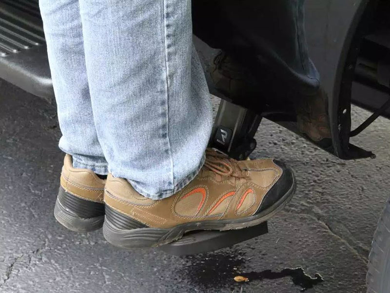 A person in jeans and work shoes stands on the deployed side bed step of a dark pickup