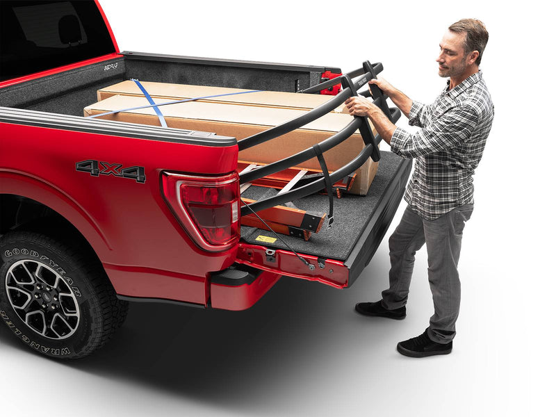 A man flips the BedXTender HD Max outward over the lowered tailgate of a red pickup loaded with boxes