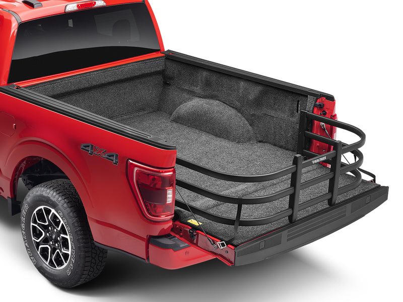 BedXTender HD Max extended over the lowered tailgate of a red crew-cab pickup, rear three-quarter studio view