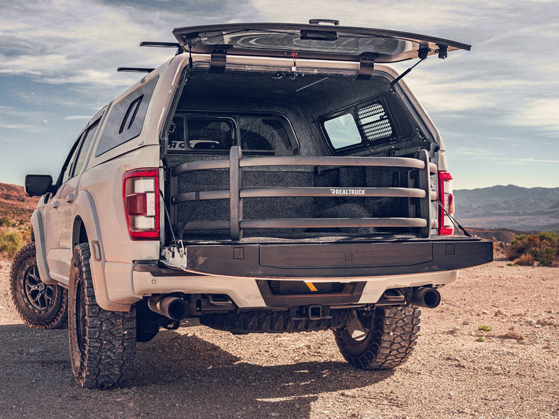 Tan off-road pickup with a camper shell parked in the desert, the bed extender deployed over the lowered tailgate