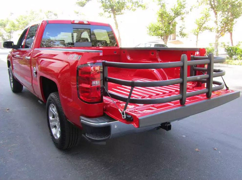 Red crew-cab pickup parked on a street with a black bed extender extended over the lowered tailgate