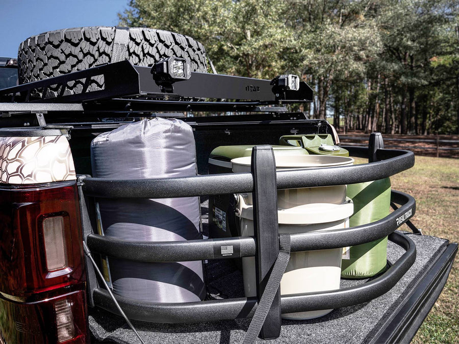 Camping gear and coolers held in place by the extended bed extender on a lowered tailgate, outdoors among trees