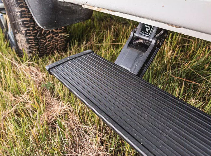 PowerStep deployed above long grass under a white vehicle