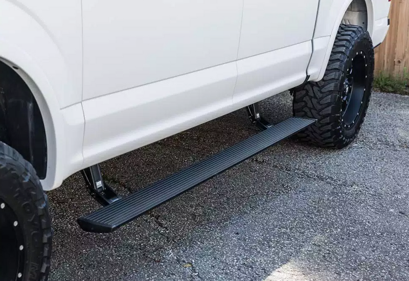PowerStep deployed under the doors of a lifted white pickup on asphalt