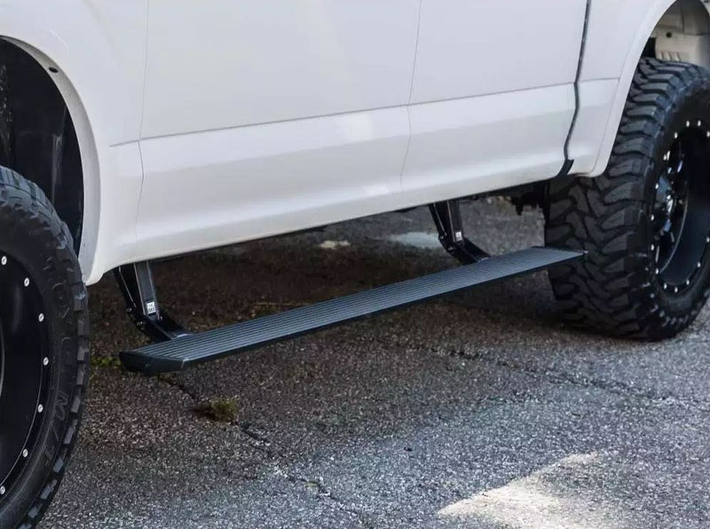 PowerStep deployed under the doors of a lifted white pickup on asphalt