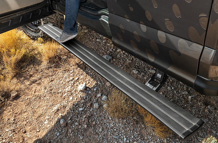A person steps down onto the deployed running board of a camouflage-wrapped vehicle in the desert