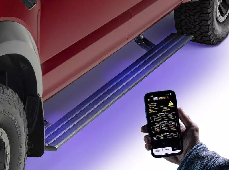 A hand holds a phone app beside the lit running board deployed under a red pickup
