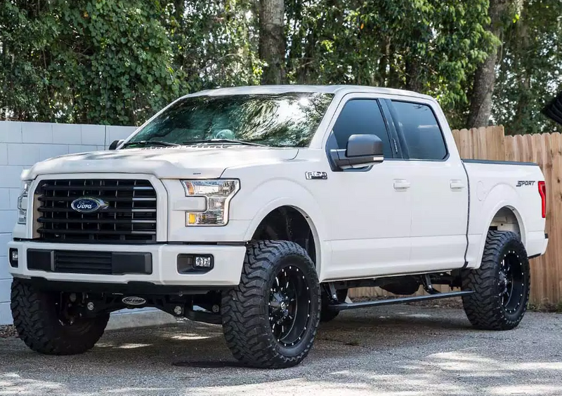 Lifted white crew-cab pickup parked by a wooden fence, front three-quarter view