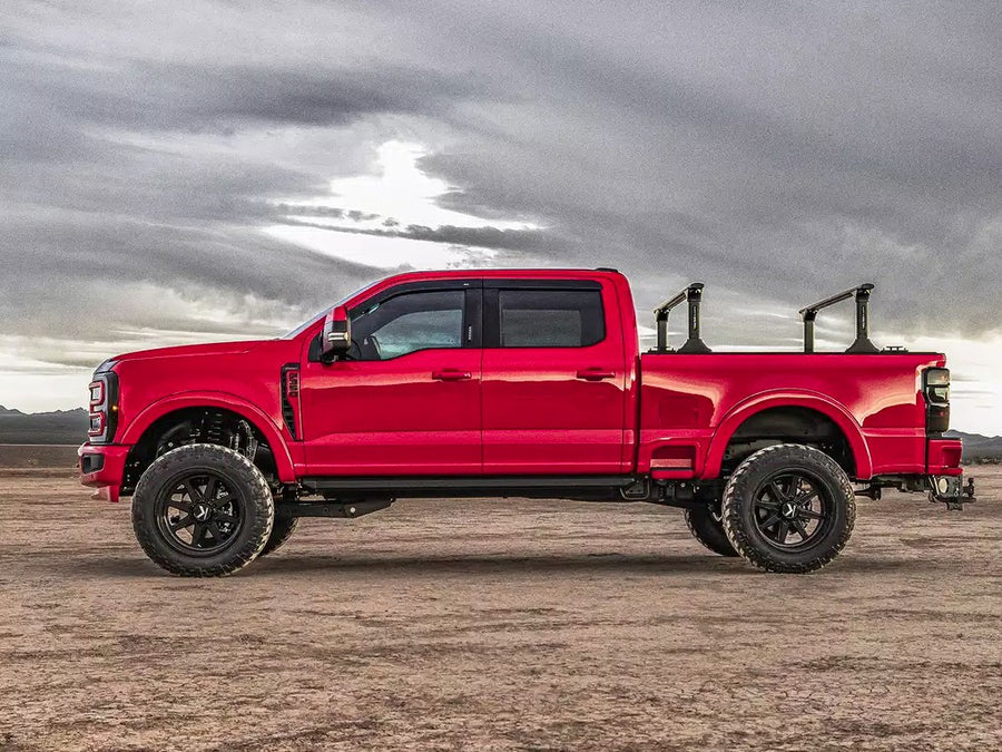 Lifted red crew-cab pickup with a bed rack parked on a desert flat under a stormy sky
