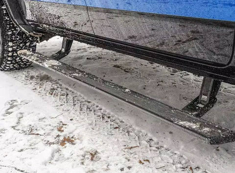 PowerStep Xtreme deployed under the doors of a mud-splashed blue pickup parked in snow
