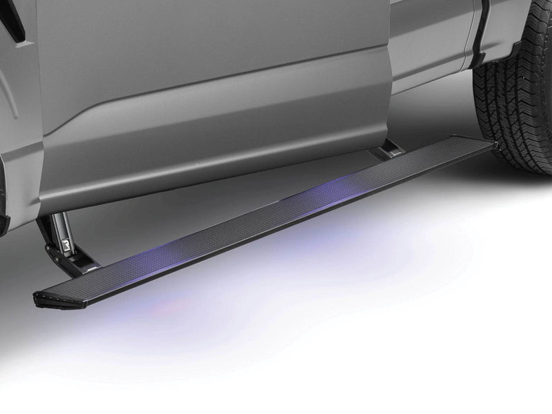 Black PowerStep Xtreme running board deployed below the doors of a silver pickup, blue under-glow lighting the ground, studio.