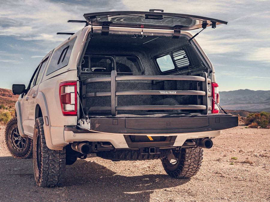 Tan off-road pickup with a camper shell parked in the desert, the bed extender deployed over the lowered tailgate