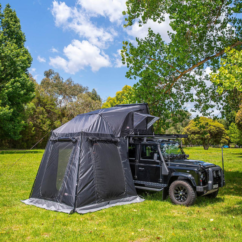 ARB Esperance V2 Annex 804200V2 fully pitched under a rooftop tent on a black Defender at a grass campsite, guy lines pegged and floor laid out