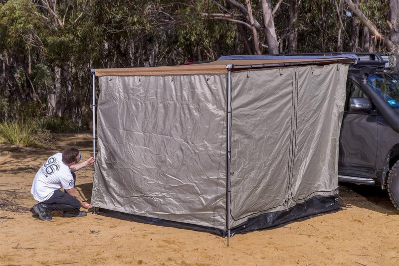 ARB Deluxe Awning Room with Floor being pegged out under a vehicle awning on a grey 4WD in bushland, showing the greige walls and black waterproof floor