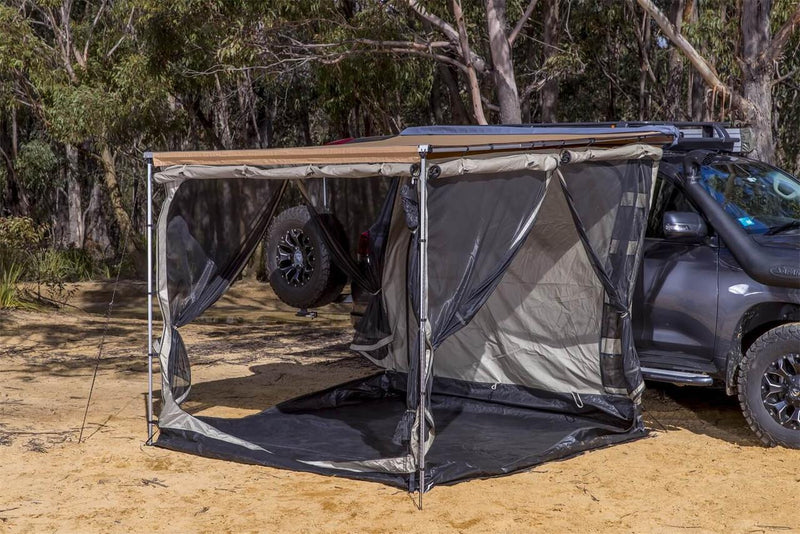 ARB awning room pitched off a grey 4WD with the mesh front open and the black waterproof floor laid flat on sand, poles and guy lines tensioned