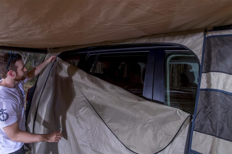 Man zipping the ARB Awning Room 813208A wall panel against a 4WD body, shown from inside the room under the awning