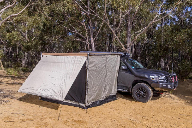 ARB Awning Room with Floor 2.0M 813208A in solid-wall configuration pitched off a grey Land Cruiser, guy lines pegged into sandy ground